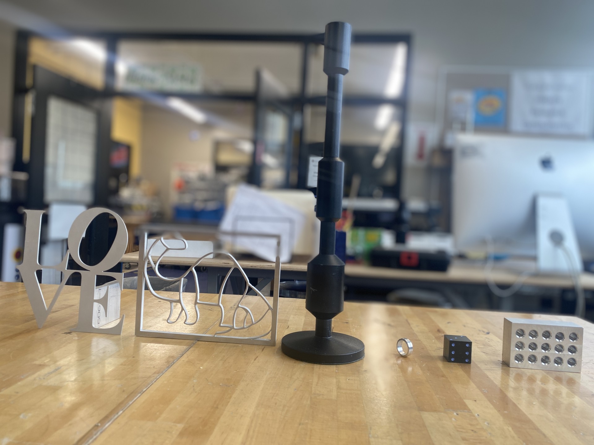 From left to right, the projects are displayed in the following order: the first two (a “Love” sign and a dinosaur) were made on the water jet; the next two (a candlestick and a ring) were turned on the lathe; and the final two (a 1x1x1 die and a 1-2-3 bl