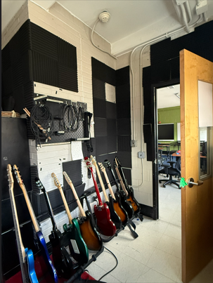 the entryway of the improved band room with the pegboard, more guitars I replaced strings on and the new bass on the end of the instrument rack!